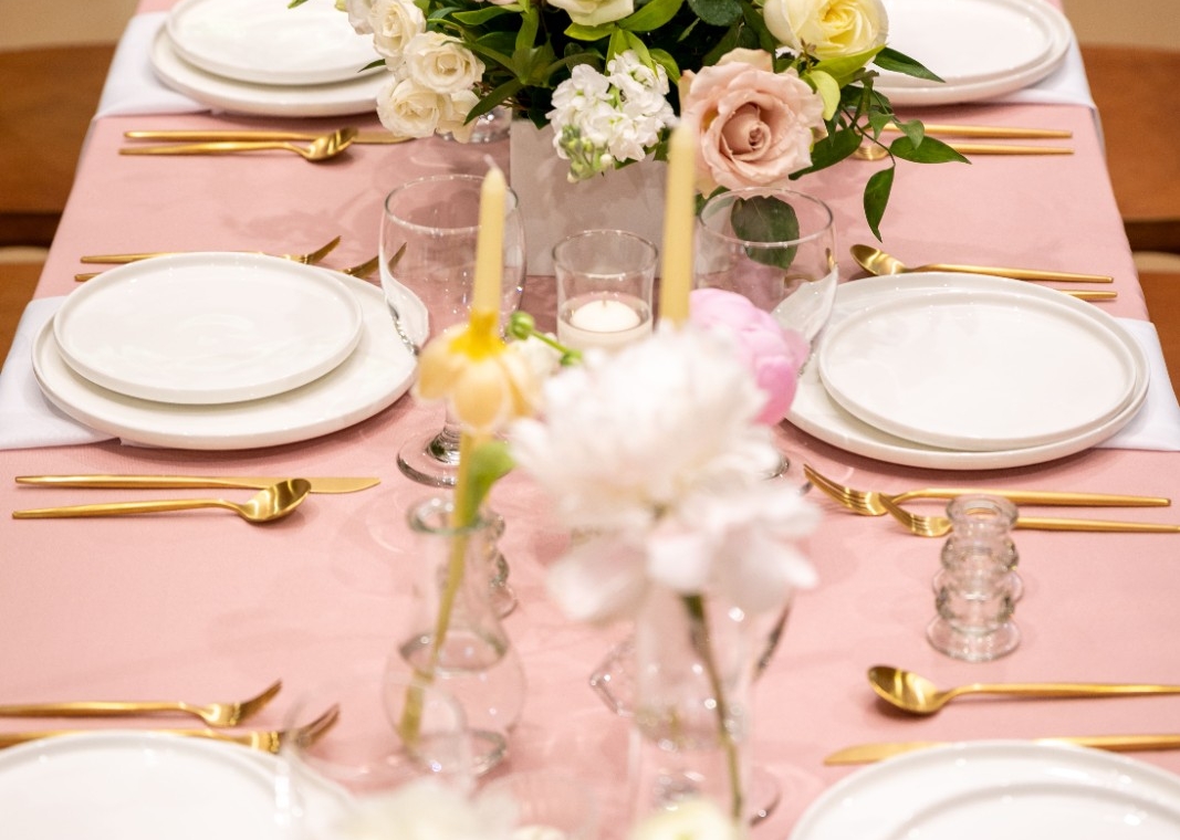 Wedding table with blush pink cloth, gold cutlery and white and peach roses in the centre