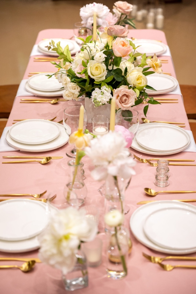 Wedding table with blush pink cloth, gold cutlery and white and peach roses in the centre