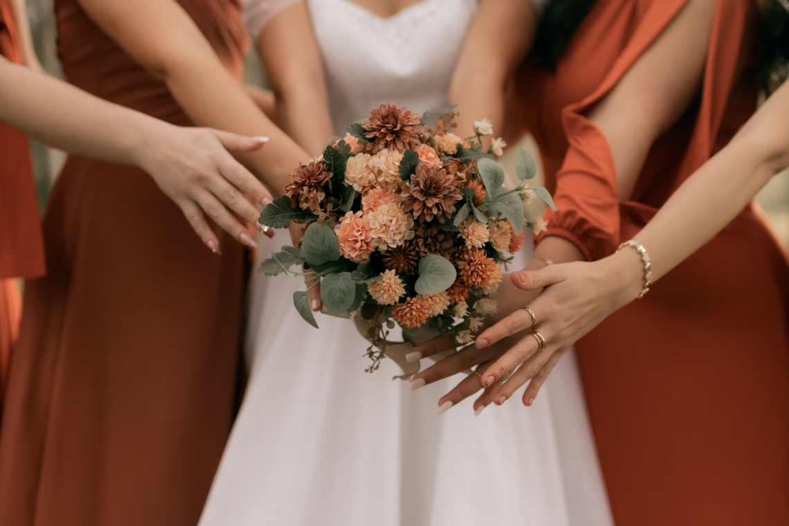 Bride and bridesmaids in terracotta dresses with hands together over an autumn bouquet