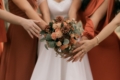 Bride and bridesmaids in terracotta dresses with hands together over an autumn bouquet