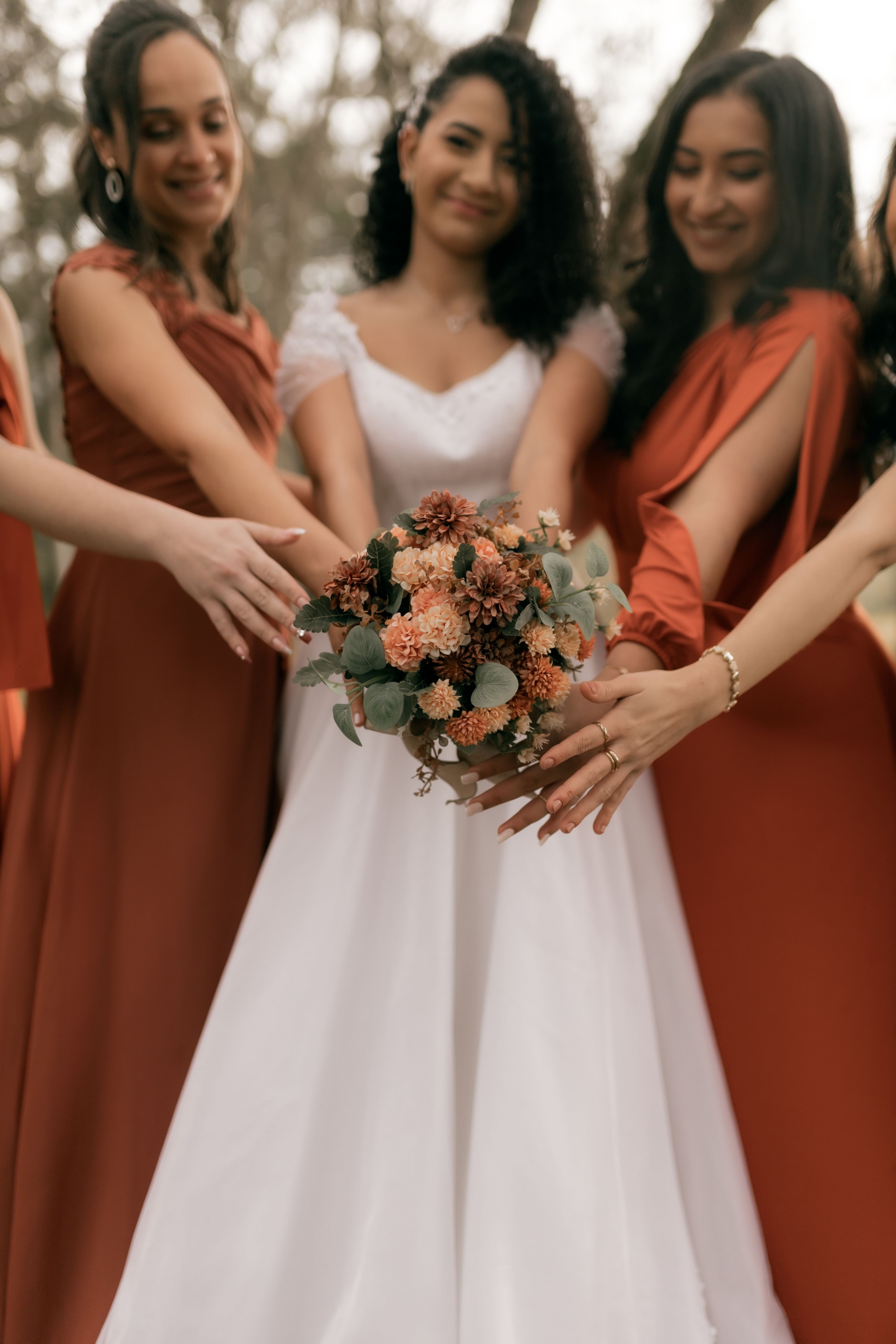 Bride and bridesmaids in terracotta dresses with hands together over an autumn bouquet