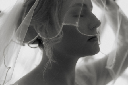 Black and white wedding portrait of a bride lifting her veil in soft window light