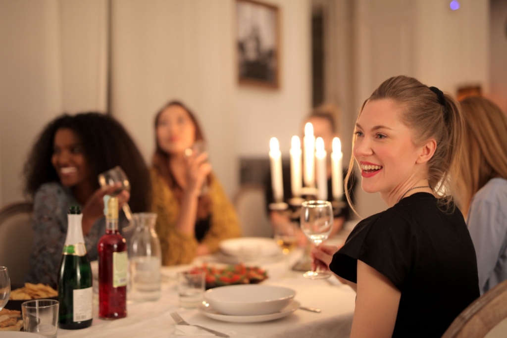 Group of friends laughing around a candlelit dinner table with wine glasses and sharing plates