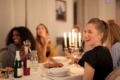 Group of friends laughing around a candlelit dinner table with wine glasses and sharing plates
